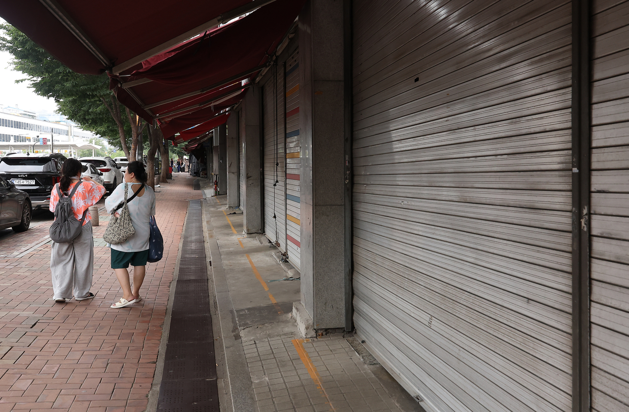 Pedestrians walk past closed shops at the Dongdaemun fashion market in Seoul’s Jongno district on Sunday, as vendors take their summer leave through Wednesday. (Yonhap)